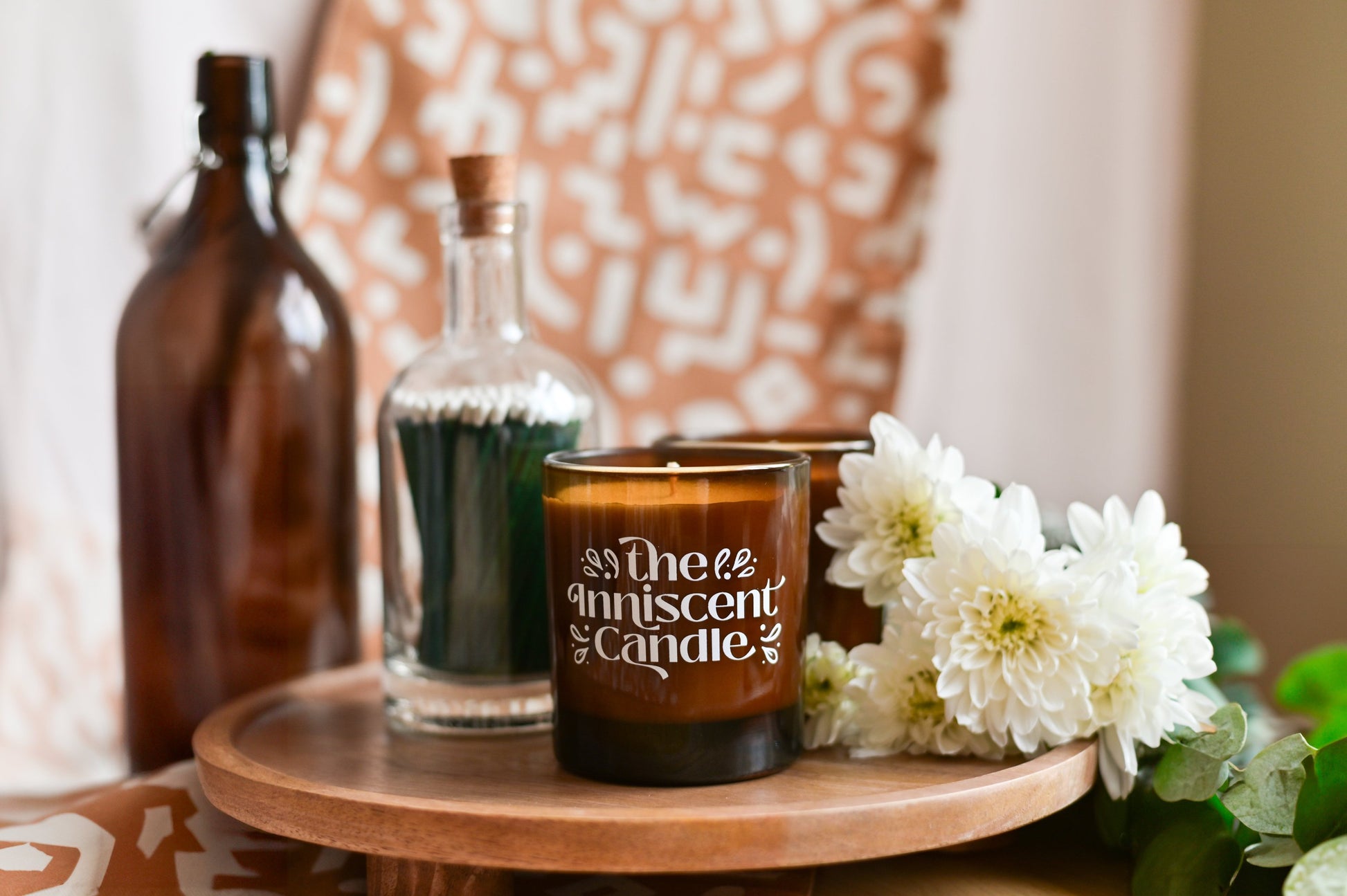 Photo of a candle with a patterned orage backdrop, beside white flowers.