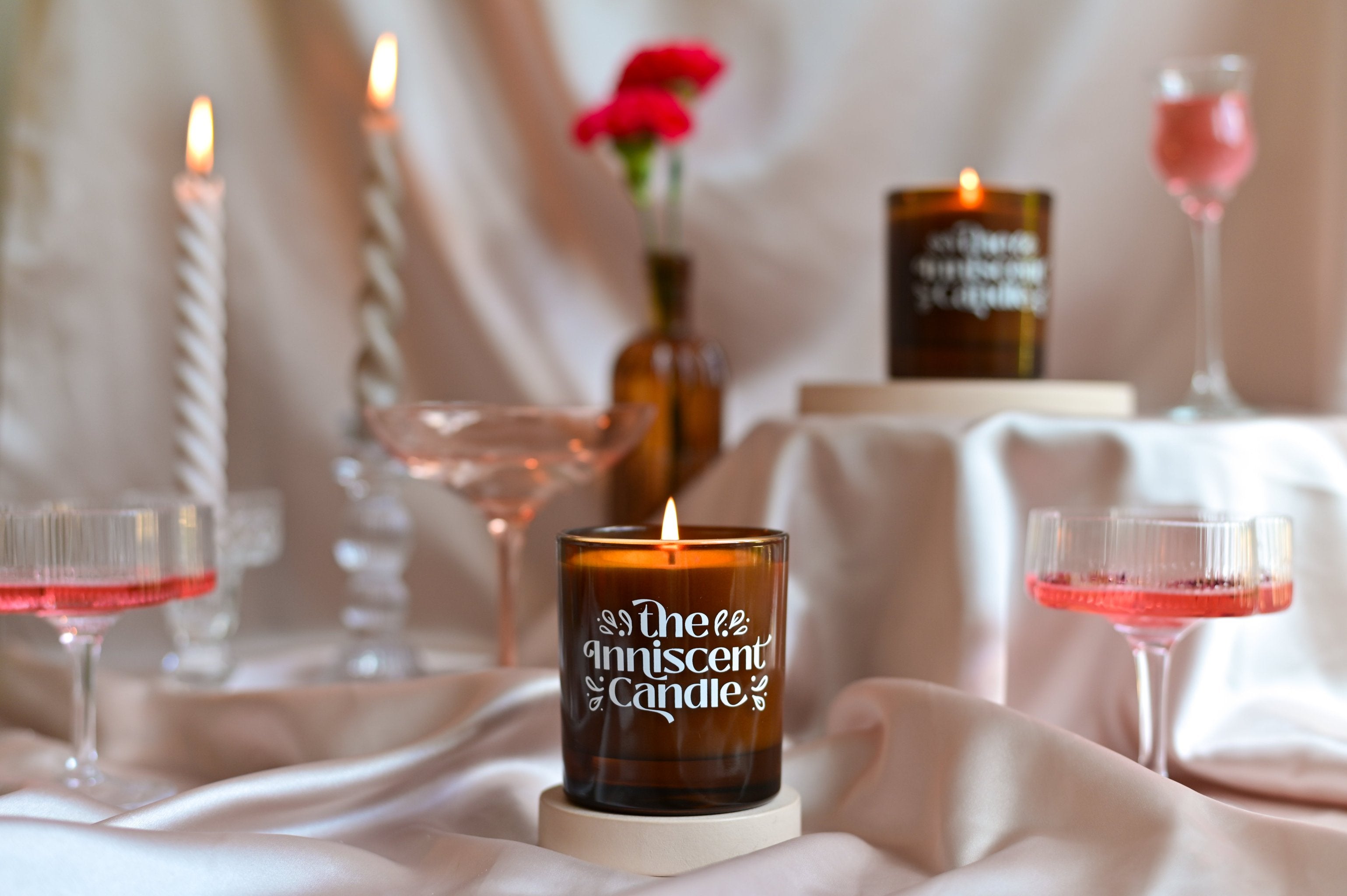 Photo of a soy scented candle with soft pink background, with cocktails and flowers.