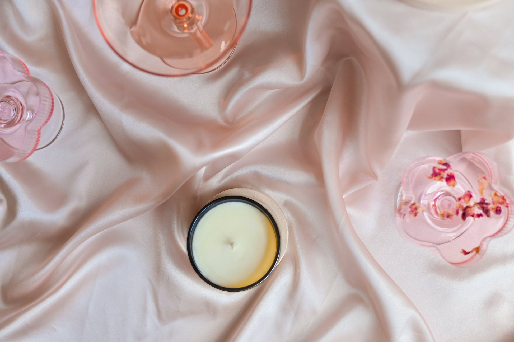 Flatlay photo of a soy candle on silky pink fabric, with cocktails.